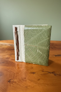 A handmade, square, green notebook with a leaf-like embossed cover and a cinnamon stick hinge.